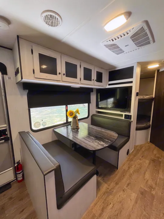 Inside a clean RV rental: a comfortable dinette, wall-mounted TV, bunk beds, and AC unit.. Heartland RVs Trail Runner 2022