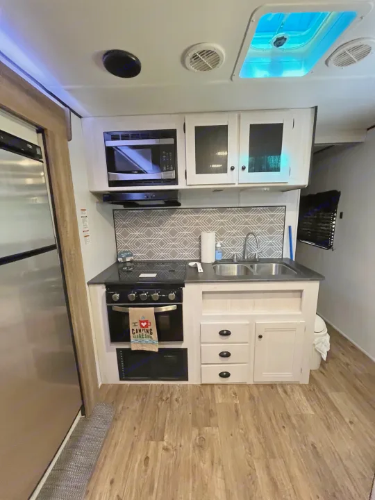 Compact RV rental kitchen with microwave, stove, sink, and fridge. Perfect for road trip camping!. Heartland RVs Trail Runner 2022