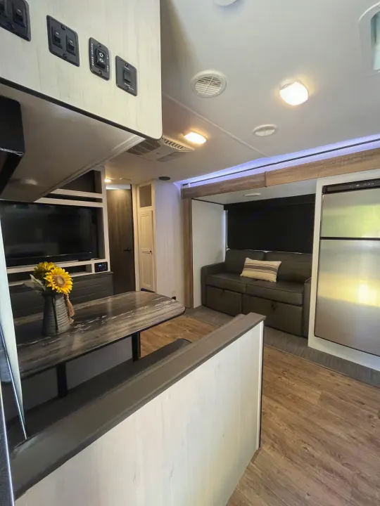 Inside a bright rv rental: dining table, TV, sofa bed, & stainless fridge in open living space.. Heartland RVs Trail Runner 2022