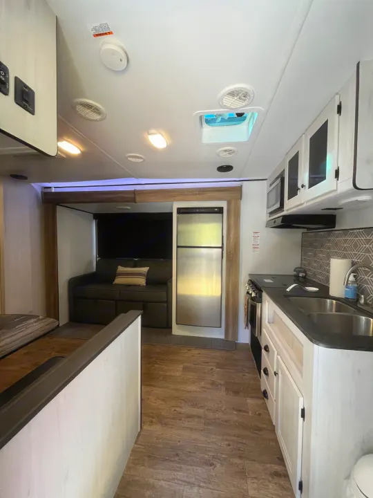 Clean rv rental kitchen and living space, featuring a full kitchen, sofa, and stainless steel fridge. Explore in comfort!. Heartland RVs Trail Runner 2022