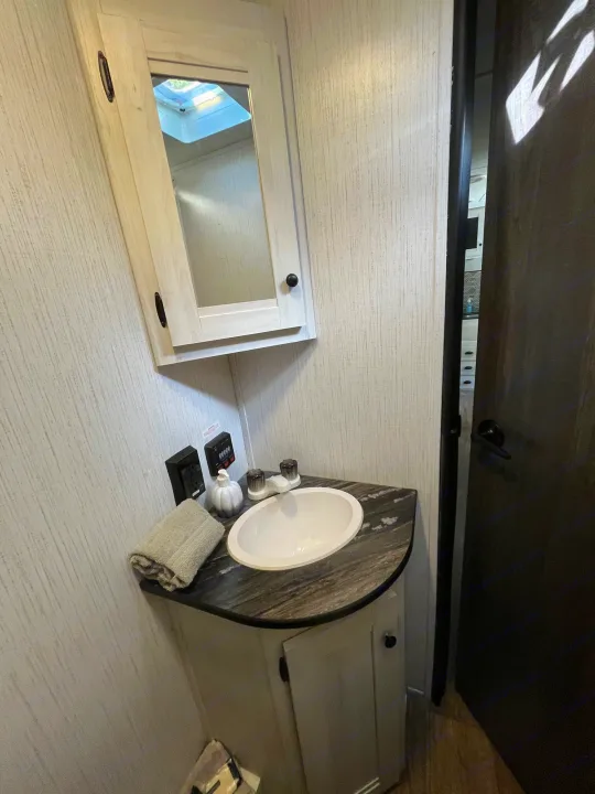 An RV rental's bathroom, showcasing a corner vanity with sink, modern white medicine cabinet, and textured walls.. Heartland RVs Trail Runner 2022