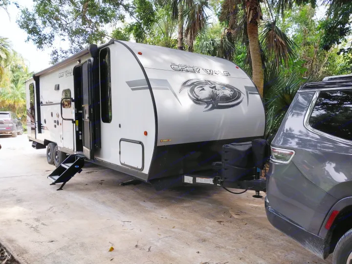 White Grey Wolf travel trailer (RV rental) hitched to a gray SUV, parked amidst trees with steps down.. Forest River Cherokee Grey Wolf Black Label 2021