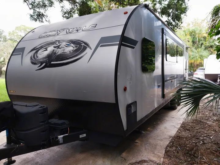 Silver Grey Wolf travel trailer (RV rental) parked on a concrete pad, showing its front, side, and propane tanks.. Forest River Cherokee Grey Wolf Black Label 2021