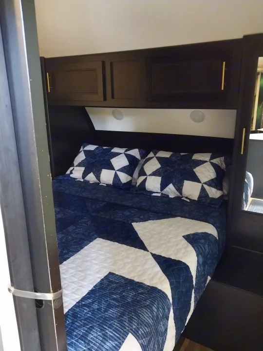Cozy RV rental bedroom with patterned blue and white bedding, overhead storage, and integrated lighting for comfortable stays.. Forest River Cherokee Grey Wolf Black Label 2021