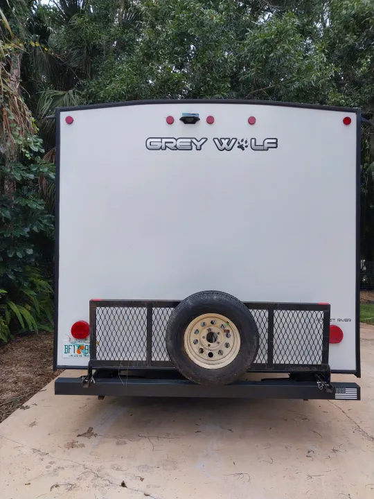Rear view of a white Grey Wolf travel trailer for rv rental, featuring spare tire, lights, and a Florida plate.. Forest River Cherokee Grey Wolf Black Label 2021