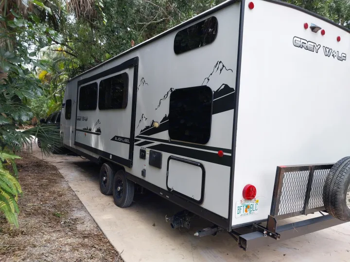 Grey Wolf travel trailer, great for rv rental adventures, parked amidst lush foliage. Features mountain graphics and spare tire.. Forest River Cherokee Grey Wolf Black Label 2021