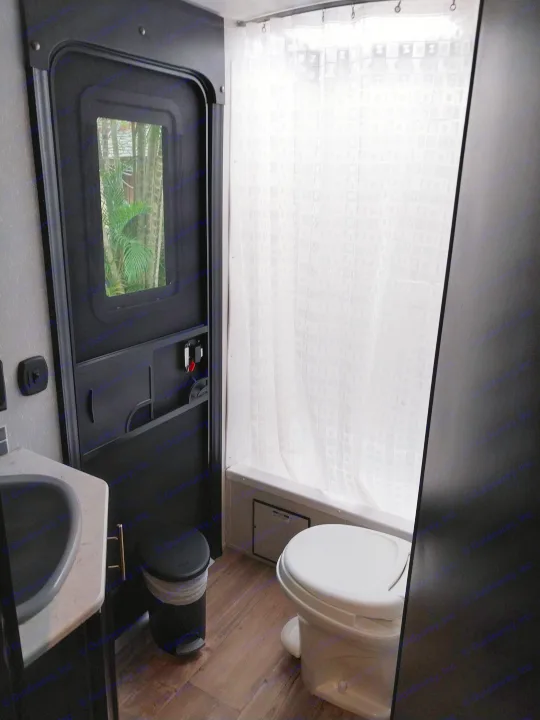 Compact RV rental bathroom with shower, toilet, sink, and outside view from door. Functional and ready for travel.. Forest River Cherokee Grey Wolf Black Label 2021