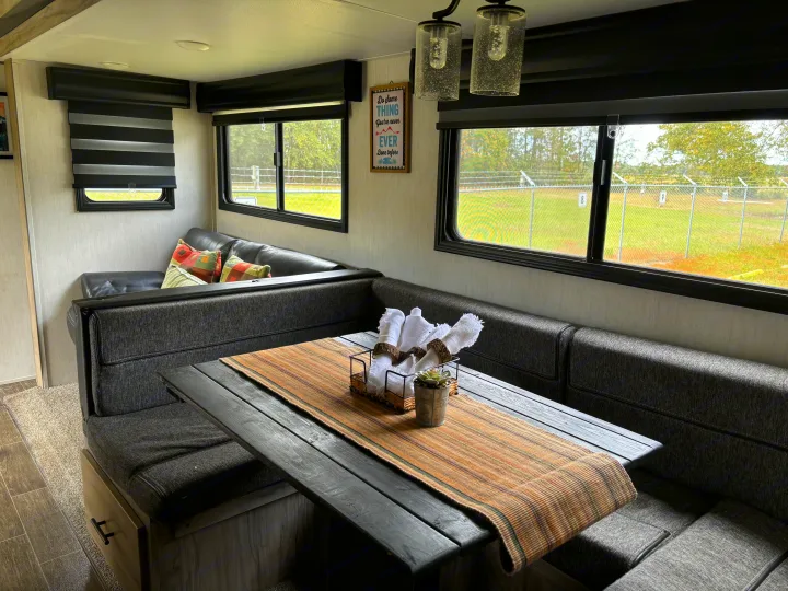 Explore comfort in this RV rental's dinette, featuring cozy seating, a rustic table, and broad windows with outdoor views.. Forest River Cherokee Alpha Wolf 2022
