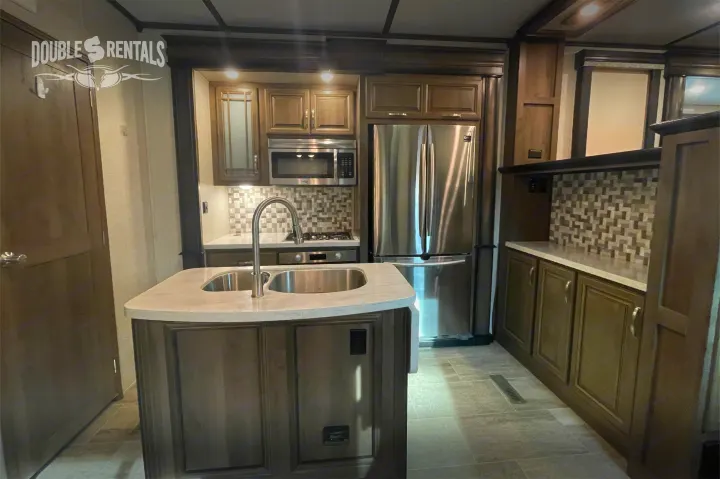 Modern RV kitchen interior with island, double sink, stainless steel appliances, and wood cabinets. Ideal for your rv rental.. Keystone Montana 2019