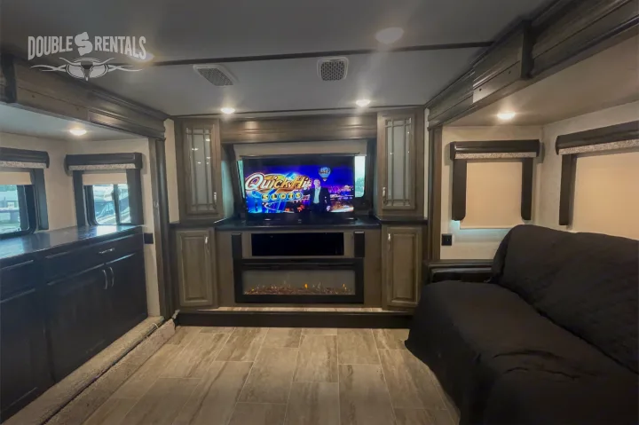 Modern RV rental living space featuring a large TV, electric fireplace, comfortable sofa, and sleek cabinetry.. Keystone Montana 2019