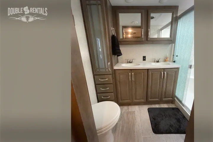 This RV rental bathroom boasts a modern double vanity, toilet, and a glass-door shower, offering comfort on the road.. Keystone Montana 2019