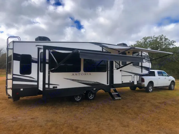 Spacious Astoria fifth-wheel RV rental, parked and set up for outdoor adventure with a truck.. Astoria 1500 2021