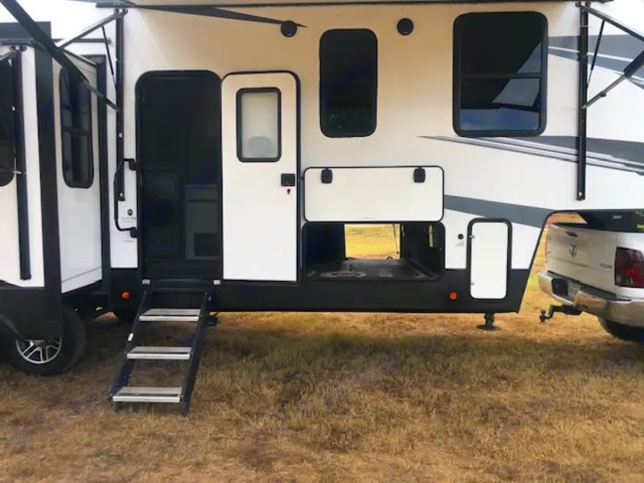 This RV rental features a white fifth-wheel trailer with extended steps, open entry, and visible storage compartments, hitched to a truck.. Astoria 1500 2021