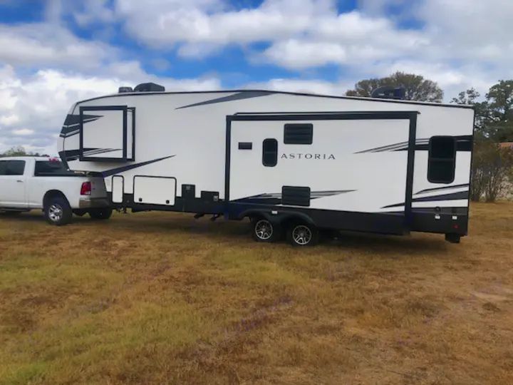 A white pickup truck hitched to a large white Astoria fifth-wheel RV sits in a grassy field. Great rv rental option!. Astoria 1500 2021