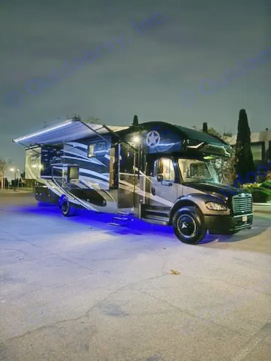 This impressive dark RV rental, a large motorhome, is shown at night with its bright awning lights and cool blue underglow.. Jayco Seneca 2020