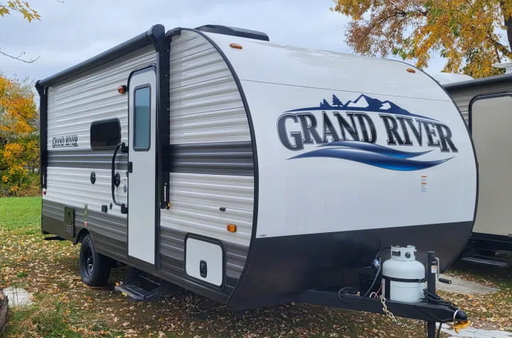 White and grey "Grand River" travel trailer parked outdoors, ready for your next rv rental adventure.. Gulf Stream Ameri-Lite 2024