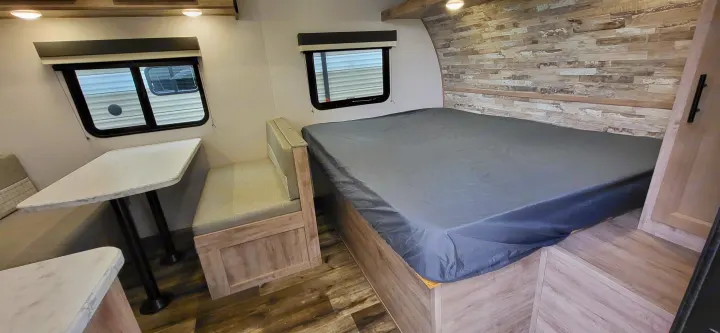 RV rental interior: modern dinette with table and benches, and a bed with a grey cover. Light wood decor throughout.. Gulf Stream Ameri-Lite 2024