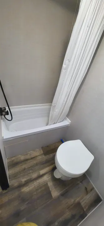 Compact RV rental bathroom: white tub/shower with curtain, toilet, and wood-look laminate floor.. Gulf Stream Ameri-Lite 2024