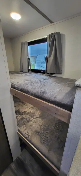 RV rental bunk beds with grey textured mattresses, window, curtains, and ceiling light visible inside a clean interior.. Gulf Stream Ameri-Lite 2024