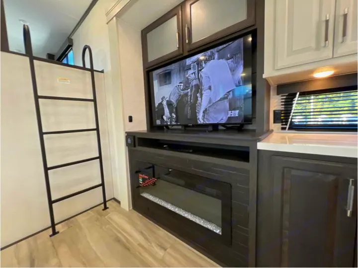 Inside a modern RV rental: TV over fireplace, ladder to bunk, and kitchen area with sink. Cozy and functional space.. Keystone Alpine 2025
