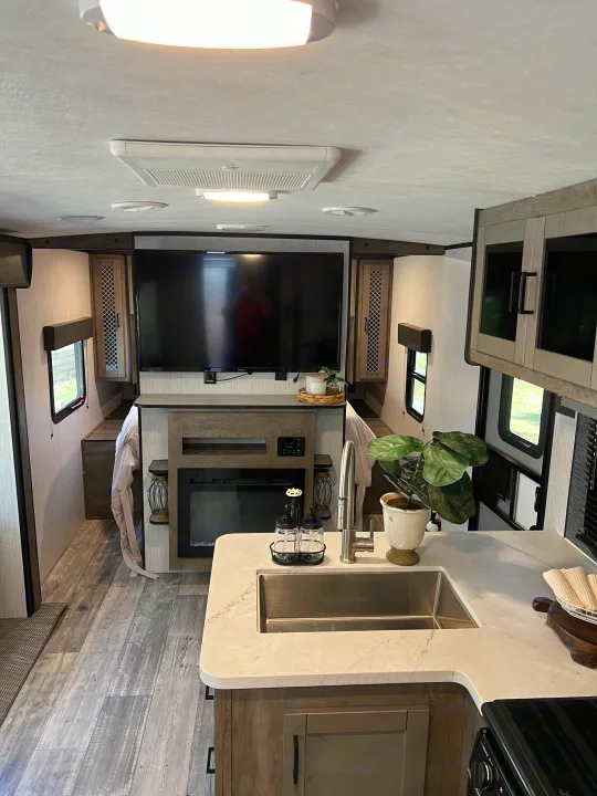 Modern RV rental interior: spacious kitchen, living area with TV & fireplace, leading to a comfy sleeping area.. Heartland RVs North Trail 2021