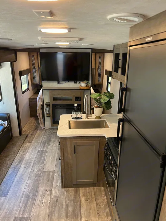 Spacious RV rental interior: modern kitchen (sink, stove, Dometic fridge), living area with TV & fireplace. Light flooring, comfortable.. Heartland RVs North Trail 2021