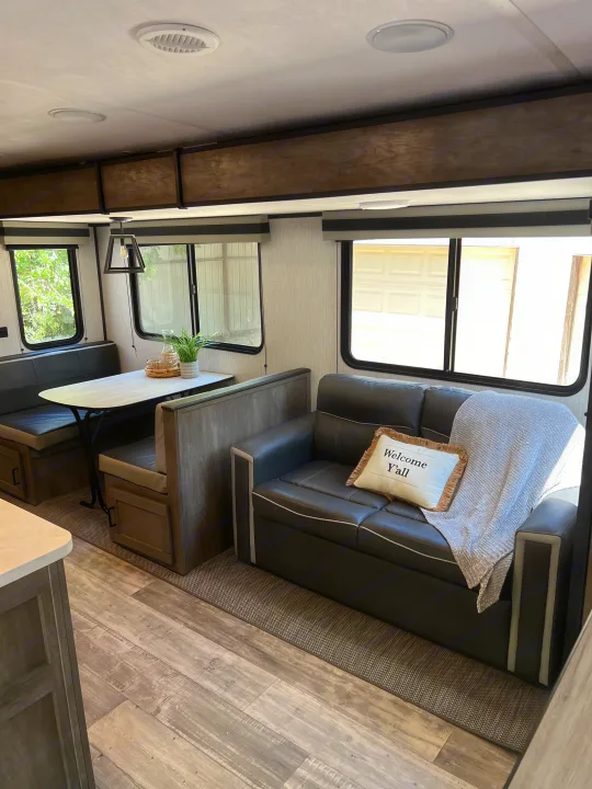 Spacious RV rental interior featuring a dining booth, comfortable sofa with a "Welcome Y'all" pillow, and modern decor.. Heartland RVs North Trail 2021