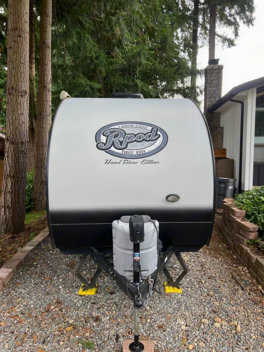 An R-Pod 'Hood River Edition' travel trailer, ideal for an RV rental, parked on gravel with trees and a house nearby.. Forest River R-Pod 2018
