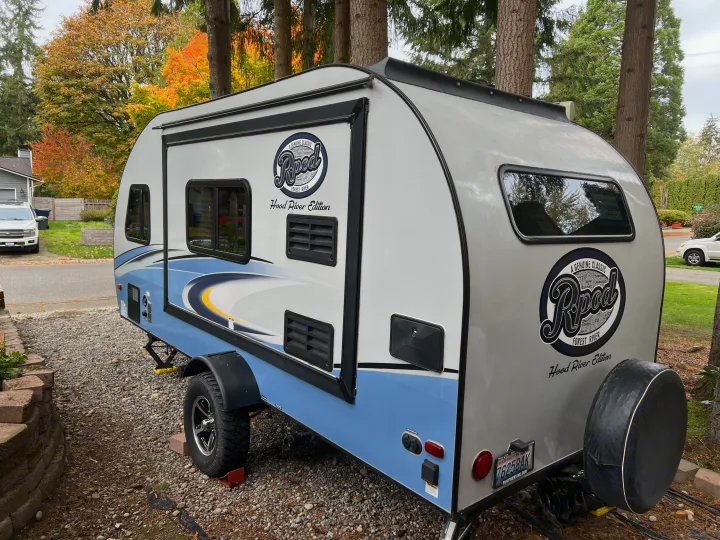 A light blue and white R-Pod camper trailer, great for an RV rental, is parked on gravel with colorful fall trees.. Forest River R-Pod 2018