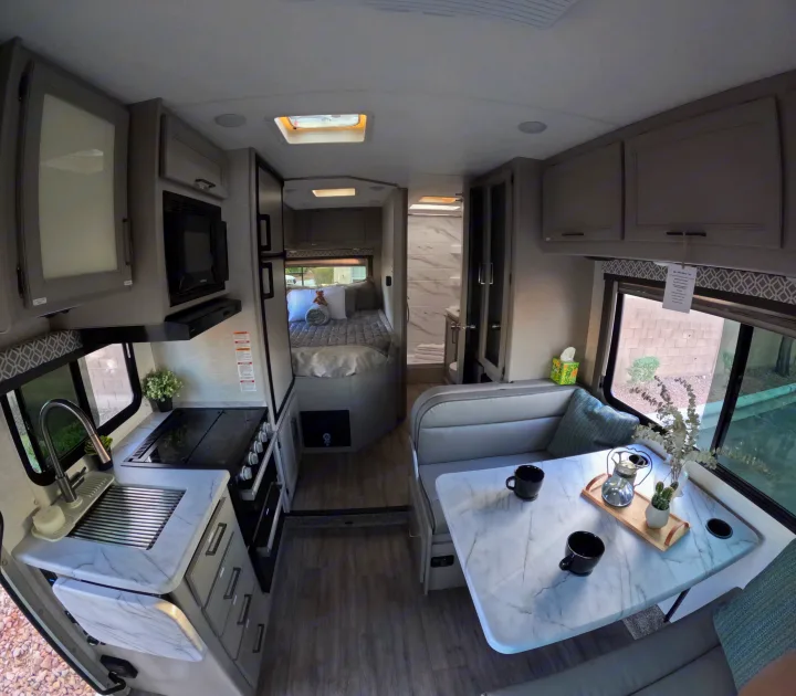 Spacious RV rental interior with modern kitchen, dining booth, comfy bed, and visible bathroom.. Thor Coleman 2024