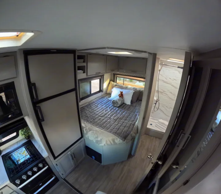 View inside a modern RV rental featuring a cozy bedroom, full kitchen with Dometic fridge, and a shower bathroom.. Thor Coleman 2024