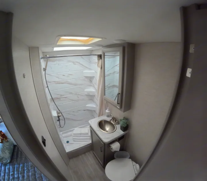 RV rental bathroom: large, tiled shower with shelves, sink vanity, toilet, and mirrored medicine cabinet. Well-lit and clean.. Thor Coleman 2024