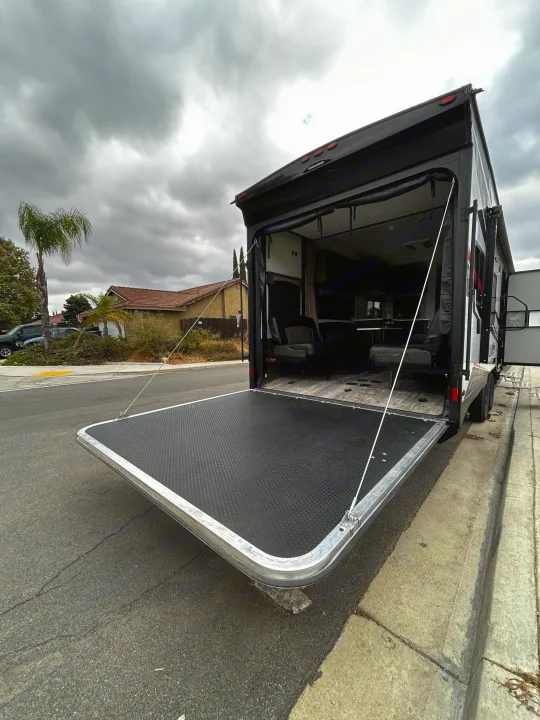 RV rental: Back of a toy hauler with its ramp lowered as a patio, parked on a residential street under an overcast sky.. Forest River Shockwave 2021