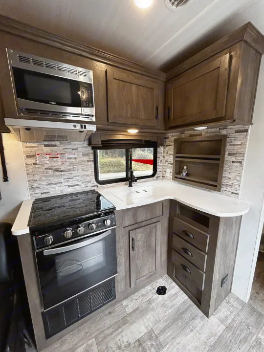 Modern RV rental kitchen featuring stove, microwave, sink, and generous counter space with stylish cabinets and backsplash.. Forest River Shockwave 2021