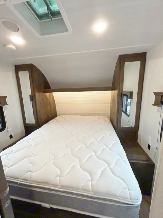 Modern RV rental bedroom with comfortable mattress, built-in headboard storage, mirrors, and ceiling lights.. Forest River Shockwave 2021