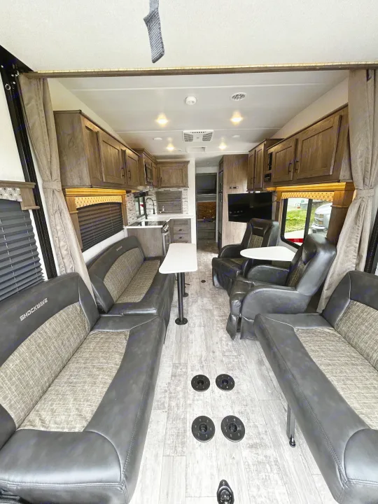 This spacious Shockwave RV rental interior features a modern kitchen, comfortable opposing sofas, and reclining chairs with tables.. Forest River Shockwave 2021