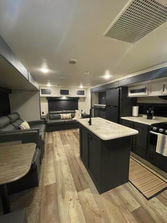 Spacious rv rental interior featuring a modern living room with sofas & a kitchen with an island & dark cabinets.. KZ Sportsmen 2022