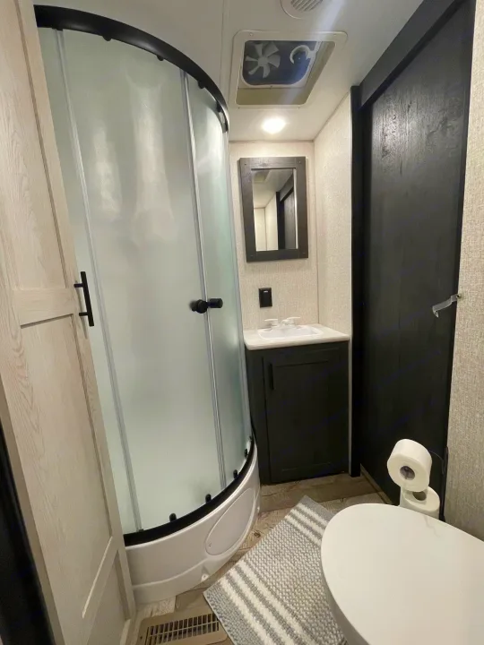 Modern RV rental bathroom with a curved frosted shower, vanity, and toilet in a space-saving layout.. KZ Sportsmen 2022