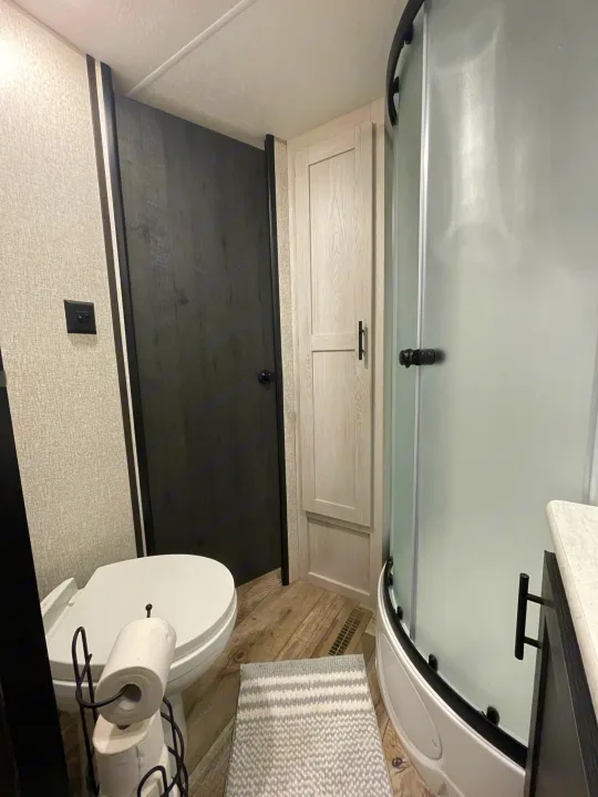 Inside an RV rental, this compact bathroom features a curved shower, white toilet, and stylish modern finishes.. KZ Sportsmen 2022