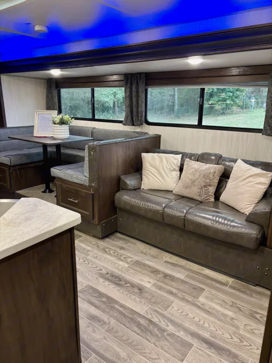 Inside your next RV rental: a modern living space with a comfy sofa, dinette, and bright blue ceiling lights.. Forest River Cherokee Grey Wolf 2019