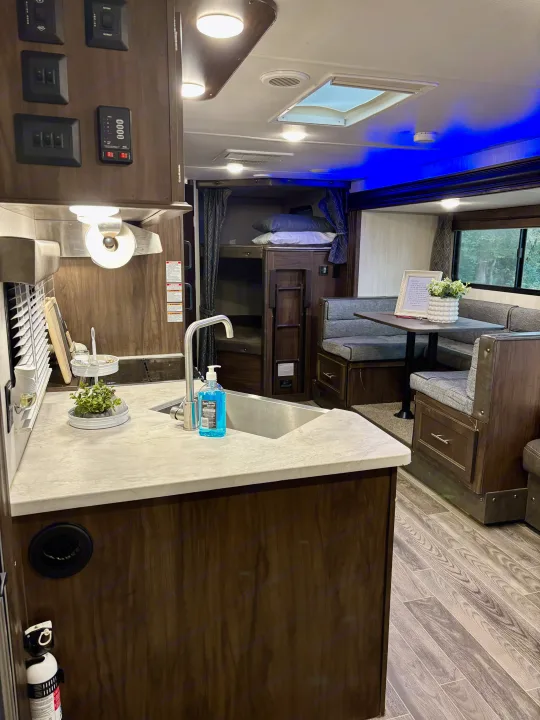 RV rental's inviting interior: light counters, dark wood cabinets, sink, dining booth, and bunk beds. Ready for adventure!. Forest River Cherokee Grey Wolf 2019