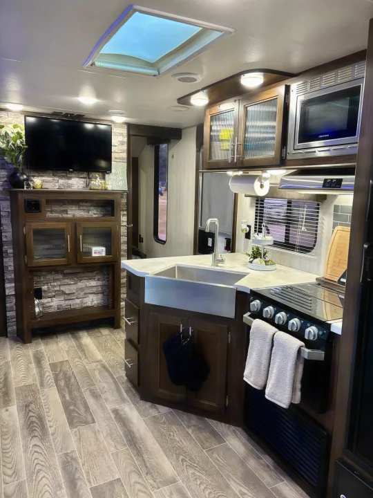 Spacious, modern rv rental kitchen and living area with a farmhouse sink, stone wall, and large TV. Ready for travel.. Forest River Cherokee Grey Wolf 2019