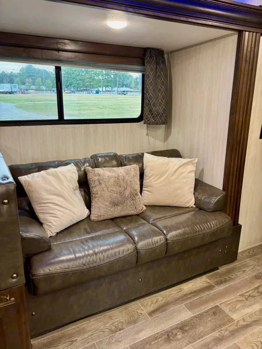 RV rental living space: leather couch with pillows, window view of a field.. Forest River Cherokee Grey Wolf 2019