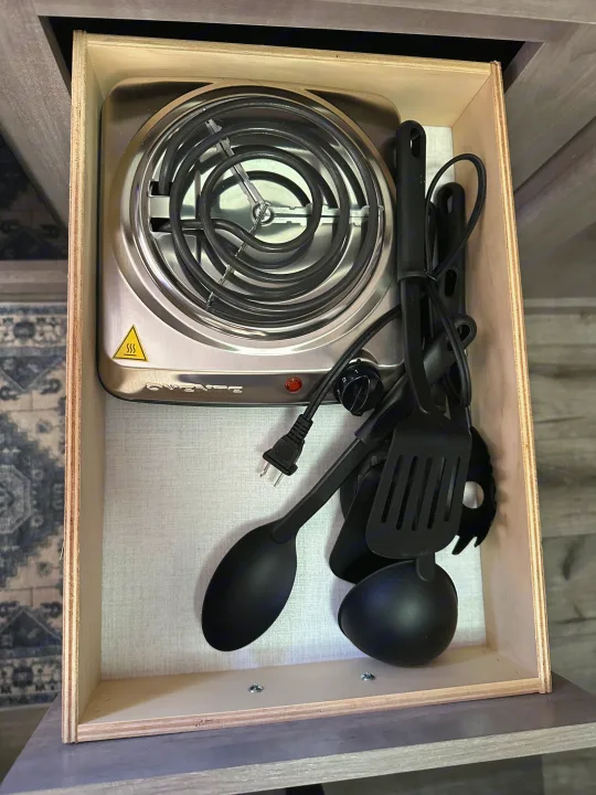 RV rental: A compact kitchen drawer with a portable electric hot plate and black cooking utensils for easy meals.. Coleman Lantern 17b 2024