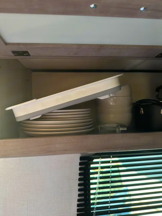 Compact RV rental kitchen cabinet storage: stacked dishes, bowls, pot, and a collapsible drying rack.. Coleman Lantern 17b 2024