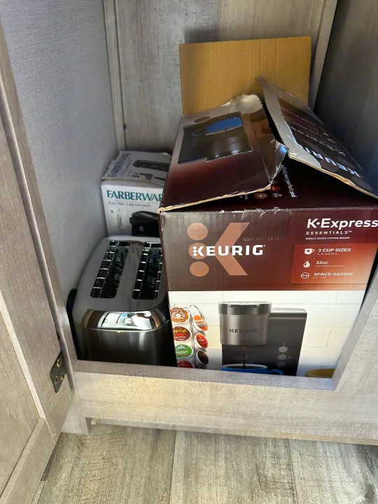 RV rental kitchen cabinet with a Keurig coffee maker, toaster, and a boxed electric can opener.. Coleman Lantern 17b 2024