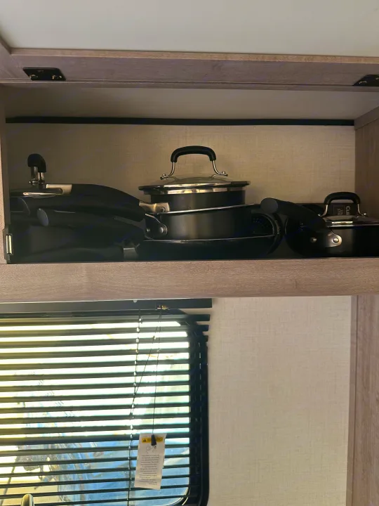 Compact kitchenware storage in an RV rental: black nesting pots & pans neatly stacked in an overhead cabinet.. Coleman Lantern 17b 2024