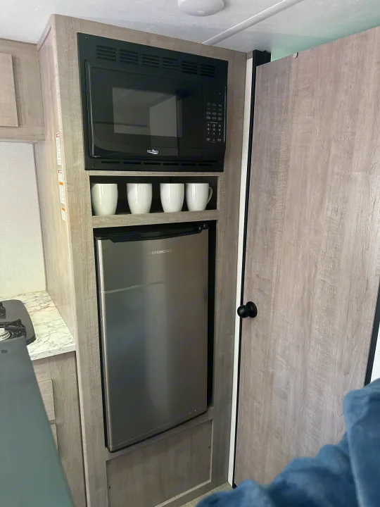This RV rental shows a compact kitchen with a High Pointe microwave, an Ever Chill mini-fridge, mugs, and a stove burner.. Coleman Lantern 17b 2024