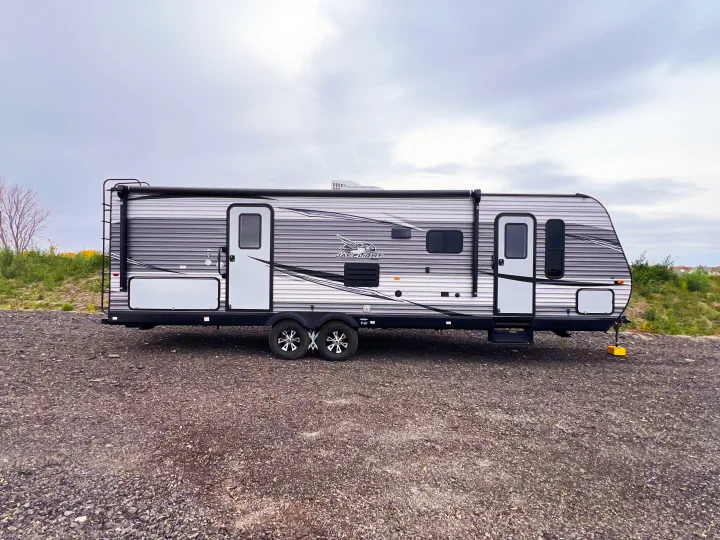 Exterior view of a modern, grey & black Jay Flight travel trailer RV rental parked on a gravel lot under a cloudy sky.. Jayco Jayflight 2021