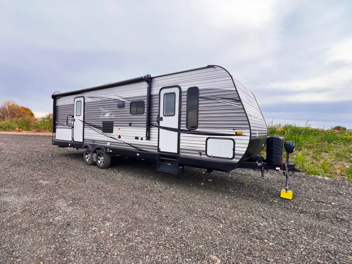 This spacious travel trailer RV, available for rv rental, is parked outdoors on a gravel lot under an overcast sky.. Jayco Jayflight 2021